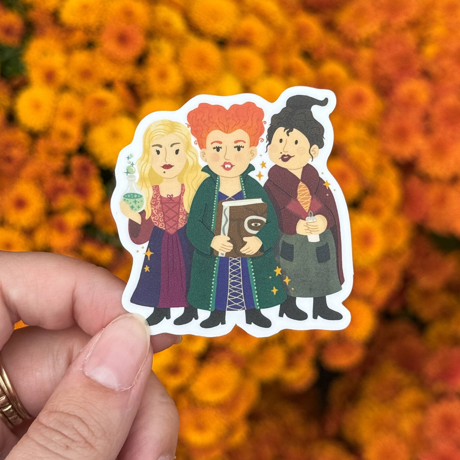 Sticker of three characters held over a background of orange flowers