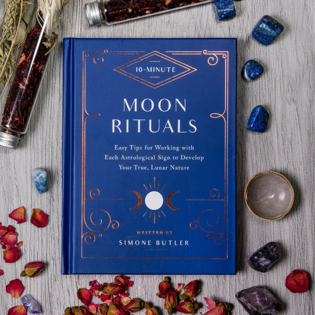 Blue book titled '10-Minute Moon Rituals' by Simone Butler on a wooden surface with dried flowers.