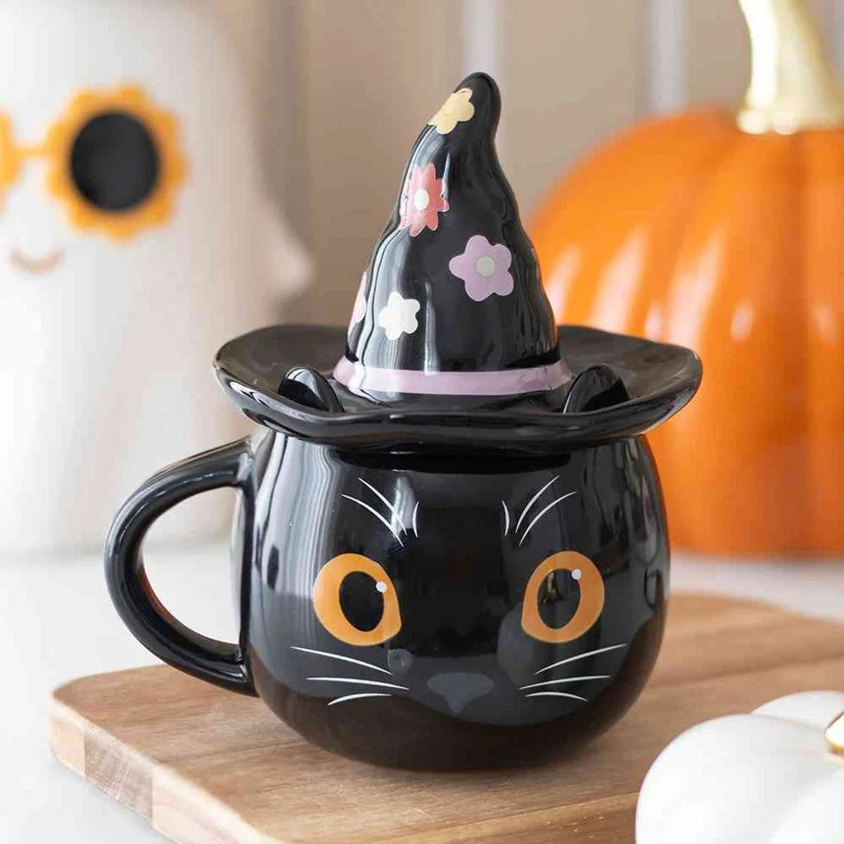 Black cat mug with witch hat on a wooden surface with Halloween decorations.