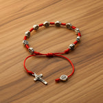 Red bracelet with silver beads and a cross on a white background