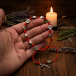Red rosary bracelet with silver beads and cross held in a hand on a white background