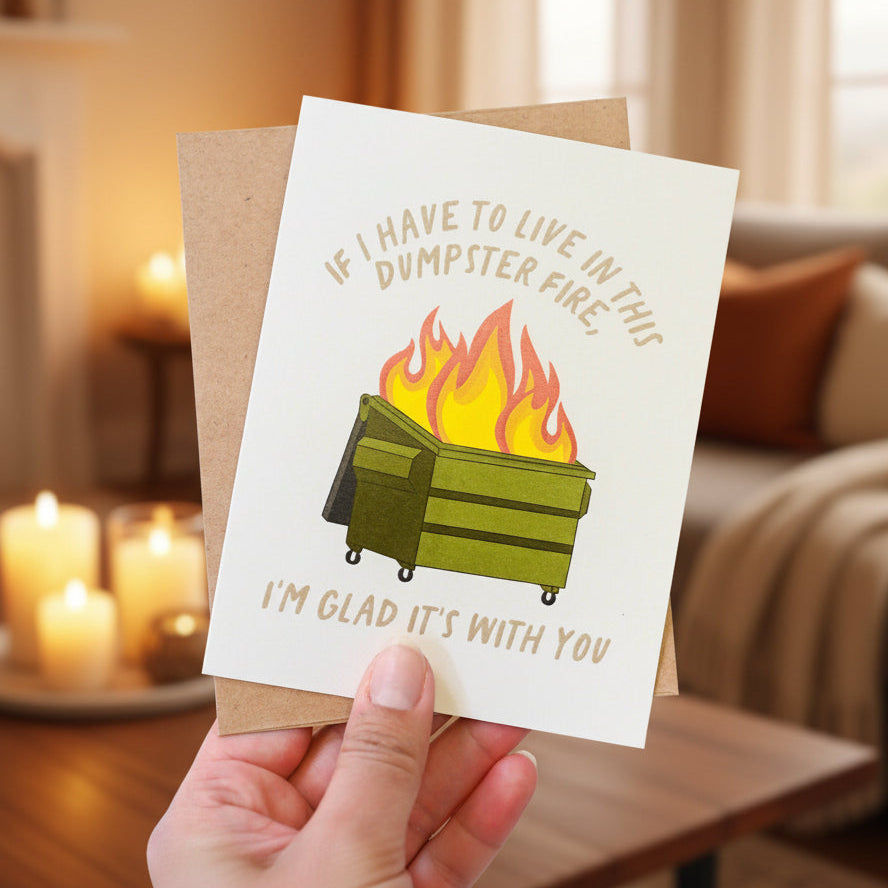 Card with a graphic of a dumpster on fire and text, held by a hand against a white background.