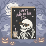 Halloween-themed card with skeleton holding a drink and text 'You're rad to the bone' against a dark background with pumpkins and ghosts.