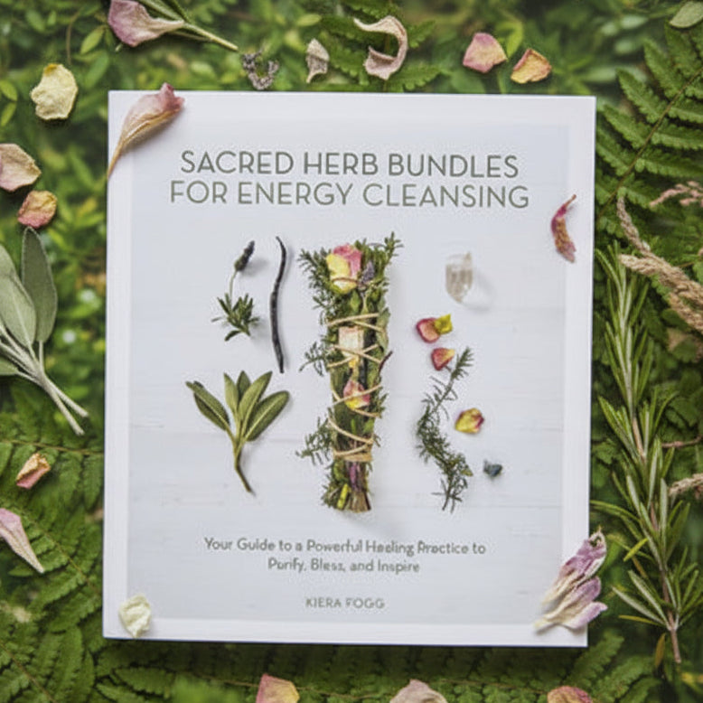 Book titled 'Sacred Herb Bundles for Energy Cleansing' on a white fabric background with dried herbs.