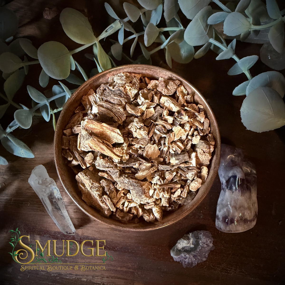Angelica root in a copper bowl on a table with eucalyptus around it.