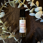 Bottle of Bergamot & Lavender perfume oil on a wooden surface with eucalyptus leaves.