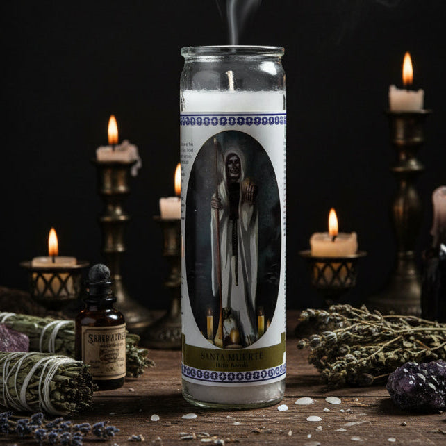 A tall glass jar candle featuring a printed label of Santa Muerte, the Holy Death, with white robes and a staff, surrounded by blue decorative borders and a gold band at the bottom.