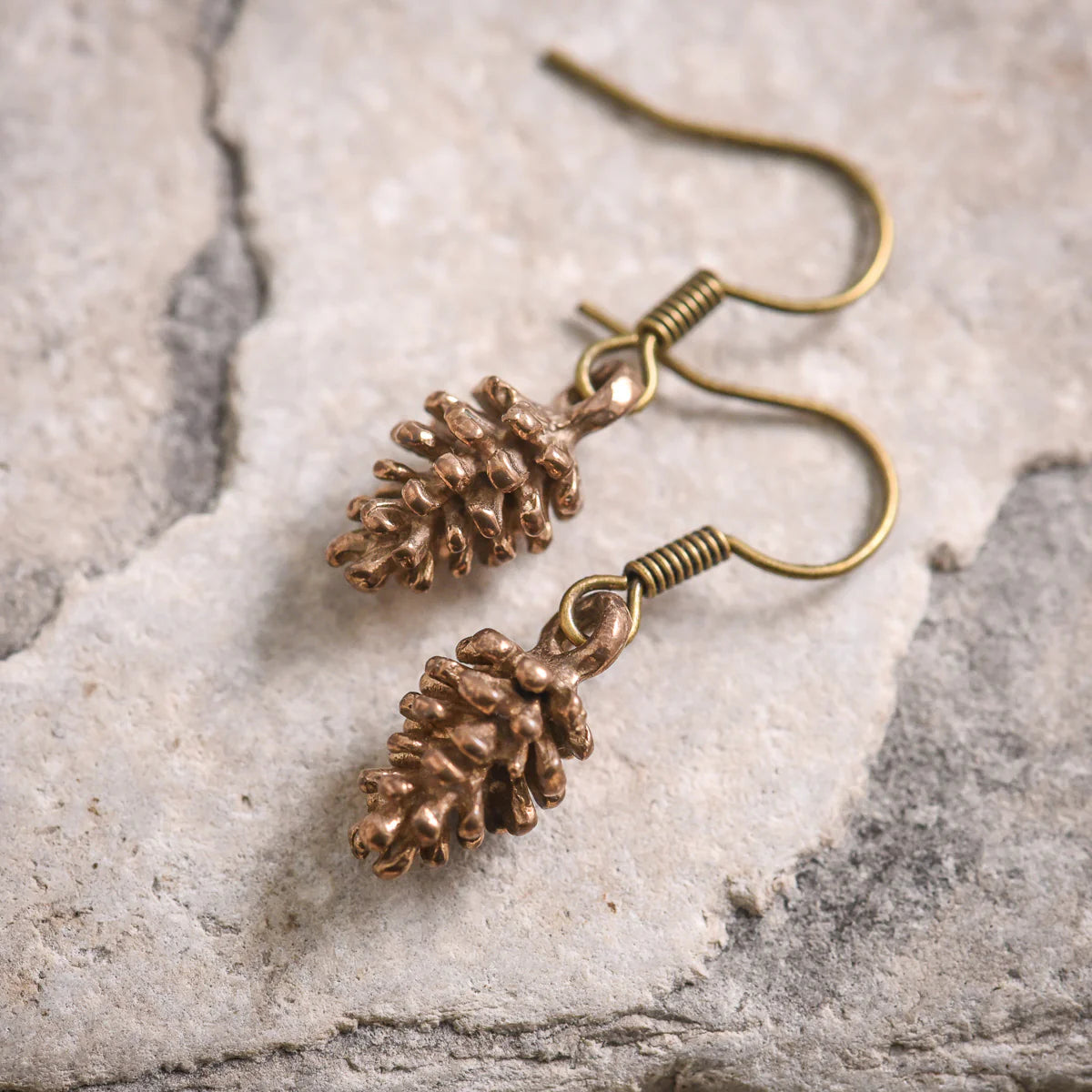 Bronze pine cone earrings on a stone surface