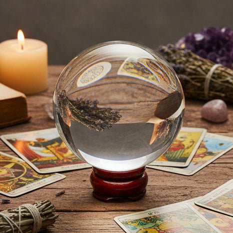 Crystal ball, candle, and smudge stick on a table with a purple cloth against a starry night sky.