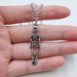 A silver skeleton pendant necklace held in a person's hand against a plain white background.