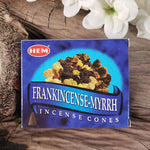 A box of HEM Frankincense Myrrh Incense Cones placed on a rustic wooden surface with white flowers in the background.