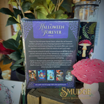The back cover of 'The Halloween Forever Oracle' card deck box is shown, featuring purple and lavender artwork with descriptive text. The box is displayed on a tabletop next to decorative mushrooms and a glass jar, with a 'SMUDGE Spiritual Boutique & Retreats' logo at the bottom.