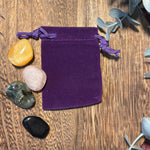 Purple velvet drawstring bag on a wooden surface with crystals and plants.