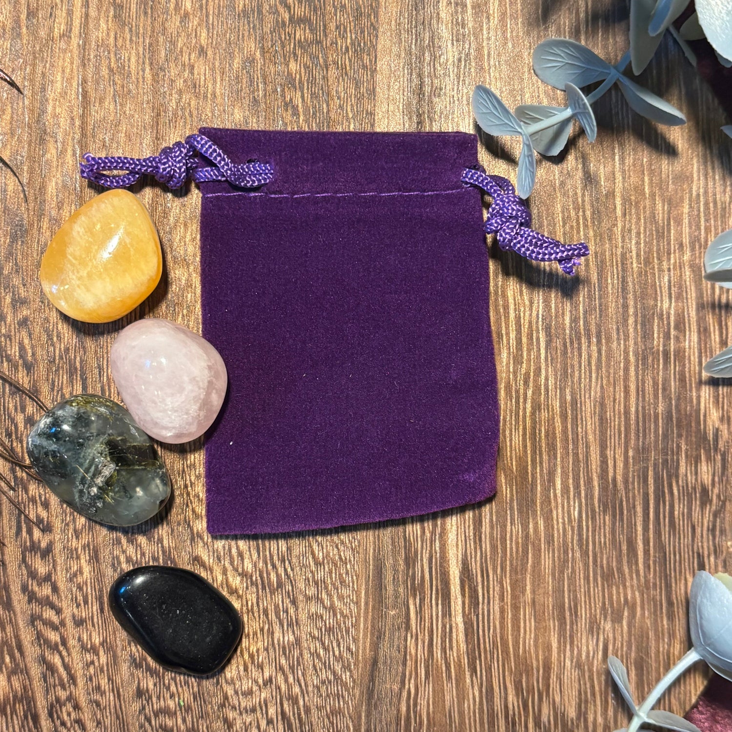 Purple velvet drawstring bag on a wooden surface with crystals and plants.