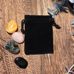 Black velvet drawstring bag on a wooden surface with crystals around it