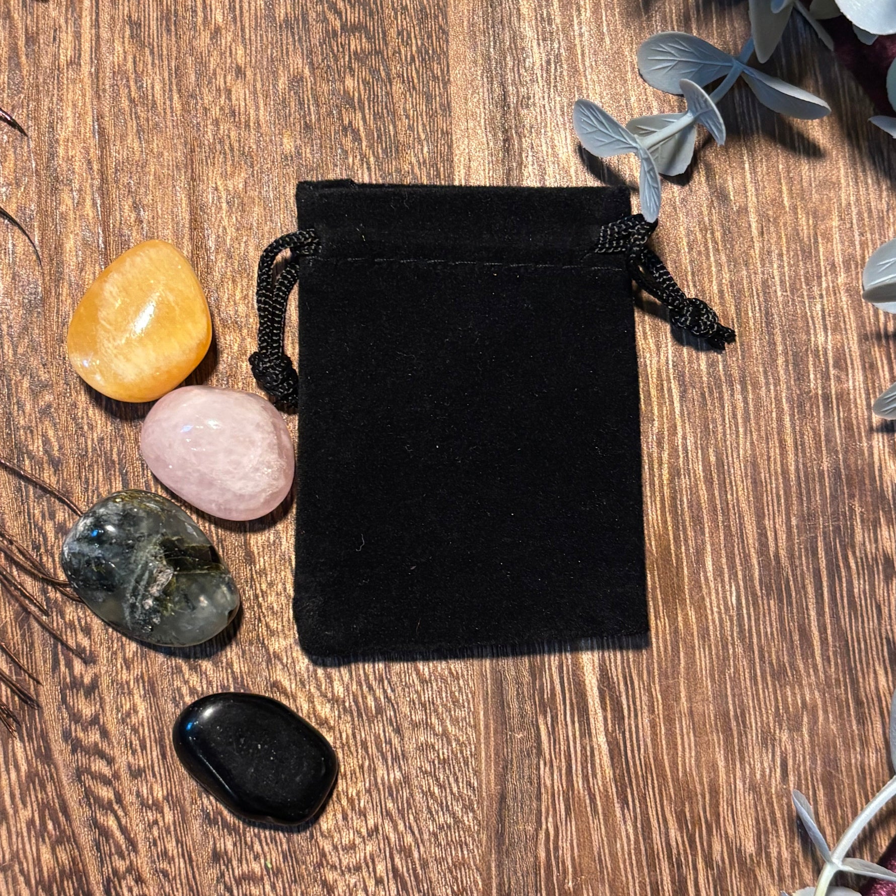 Black velvet drawstring bag on a wooden surface with crystals around it