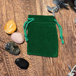 Green velvet drawstring pouch on a wooden surface with stones and leaves.