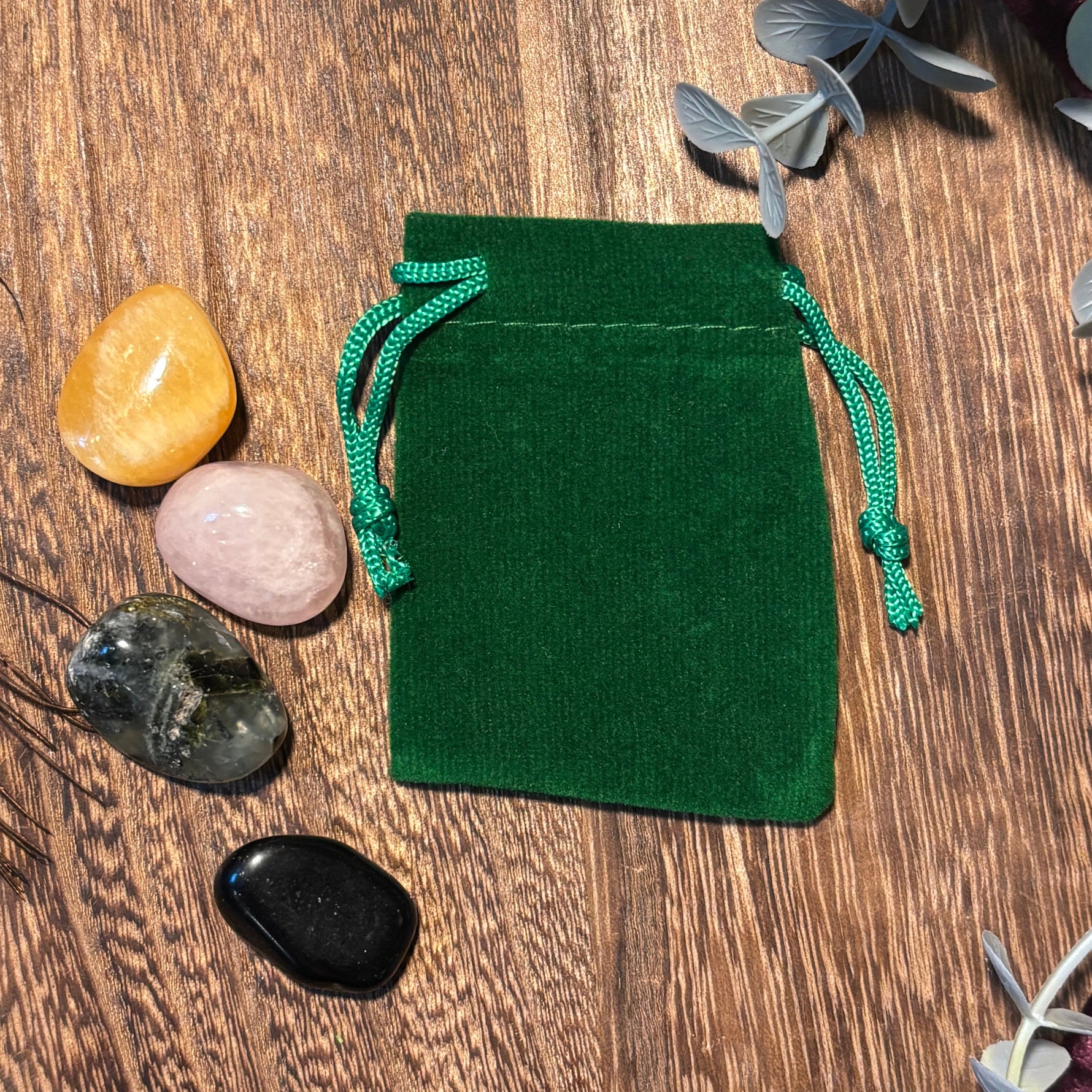 Green velvet drawstring pouch on a wooden surface with stones and leaves.