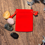 Red drawstring pouch on a wooden surface with stones around it