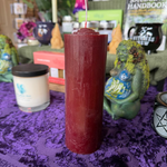 Red candle on a purple cloth with wiccan decor in the background