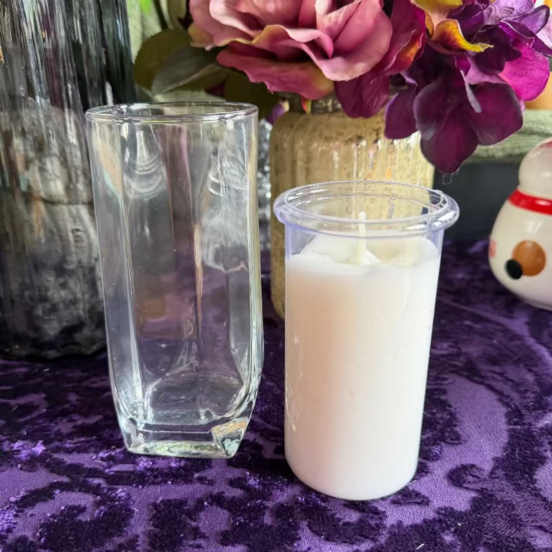 Clear glass and white candle on a purple surface with flowers in the background