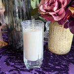 Candle in a glass holder on a purple patterned tablecloth with flowers in the background