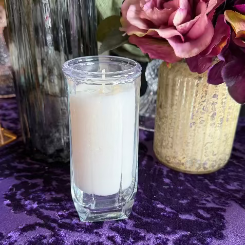 Candle in a glass holder on a purple patterned tablecloth with flowers in the background