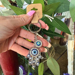 Hand holding a keychain with an owl design in front of flowers