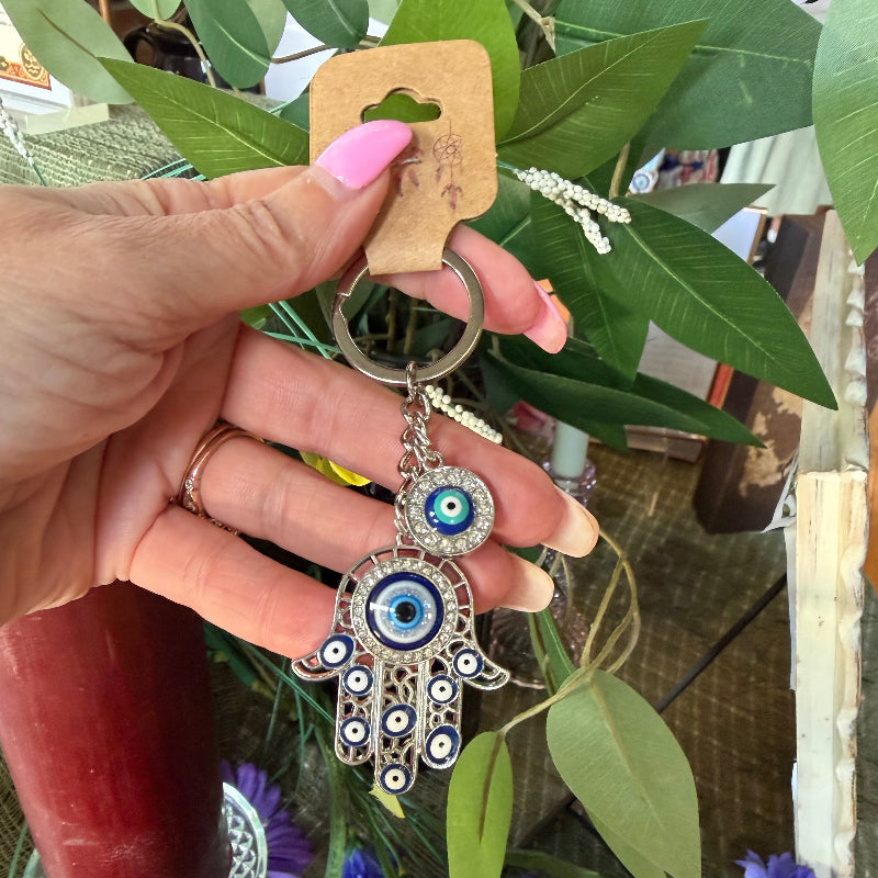Hand holding a keychain with an owl design in front of flowers