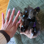 Hand with pink nail polish touching a crystal on a green surface