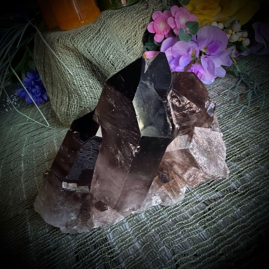Smoky quartz crystal on a textured surface with flowers in the background