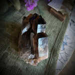 Smoky quartz crystal on a textured surface with flowers and cards in the background