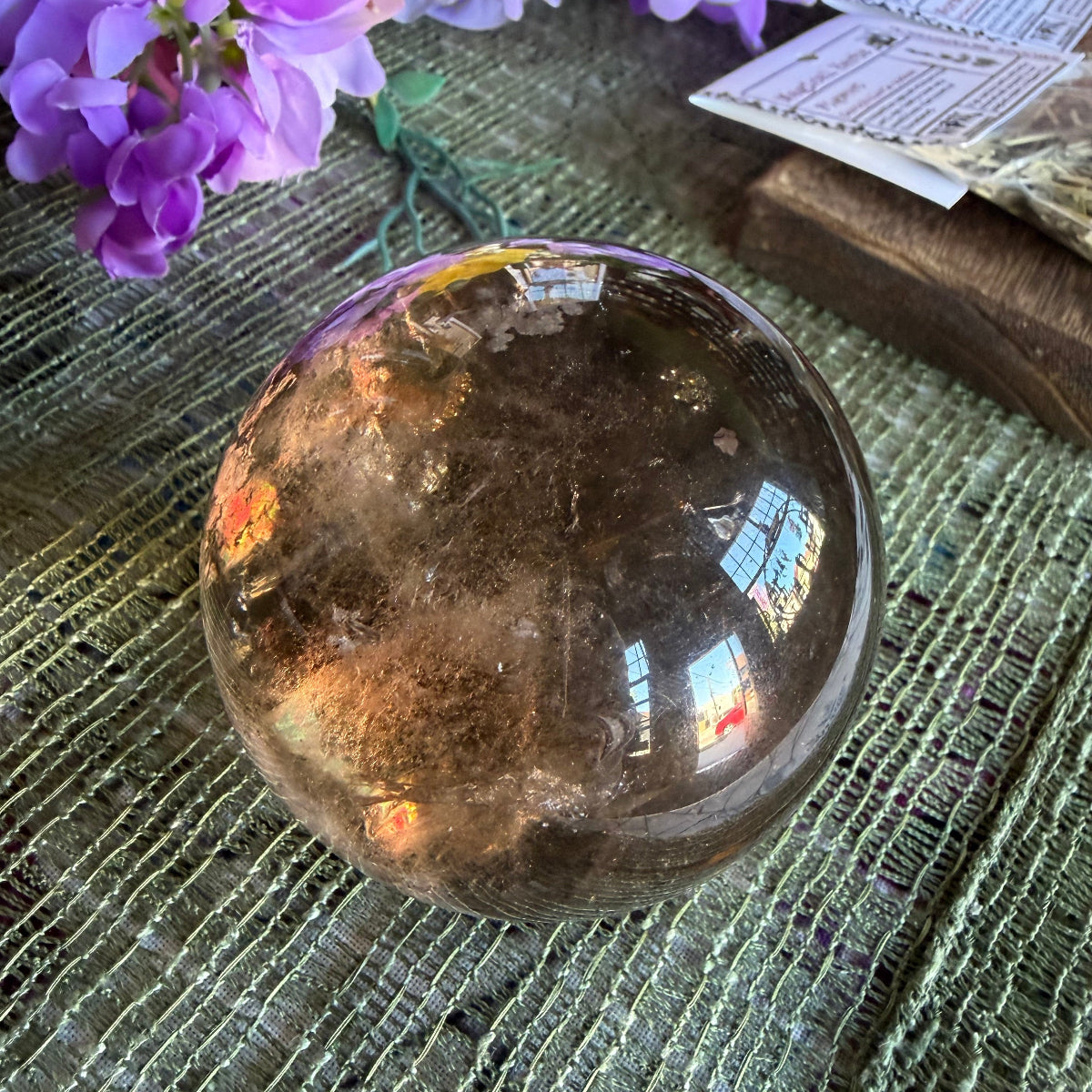 Smoky quartz crystal sphere on a textured surface with purple flowers.