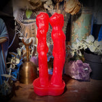 Red candle shaped like a couple on a wooden surface with decorative items in the background