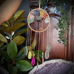 Decorative dreamcatcher with colorful beads next to a large purple crystal on a wooden surface.