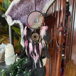 Dreamcatcher with feathers and beads on a wooden surface with plants and a cabinet in the background