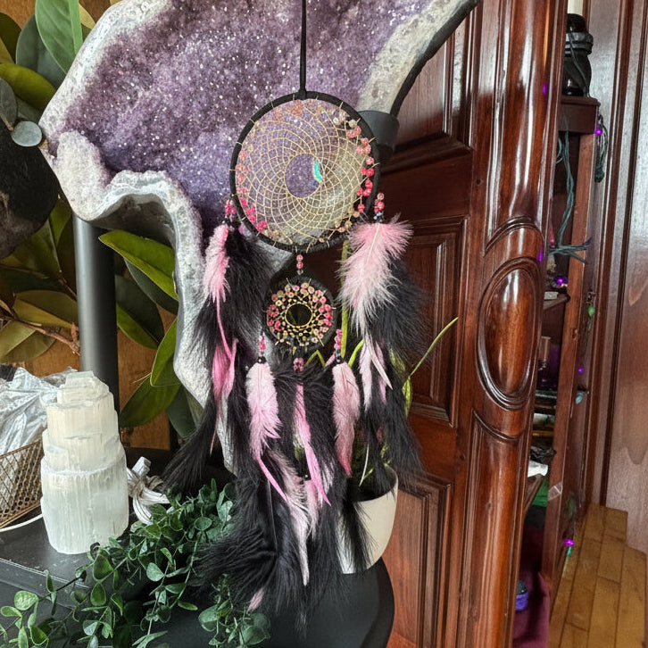 Dreamcatcher with feathers and beads on a wooden surface with plants and a cabinet in the background