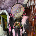 Decorative dreamcatcher with feathers against a textured wall.