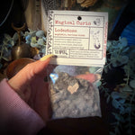 Hand holding a small package of lodestone with a label in front of decorative items.