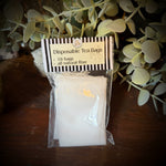 Disposable tea bags in a clear package on a wooden surface with green leaves.