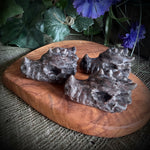 Decorative stone sculpture on a wooden base with purple flowers and greenery.