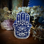 Decorative blue Hamsa hand with plants and a crystal on a wooden surface