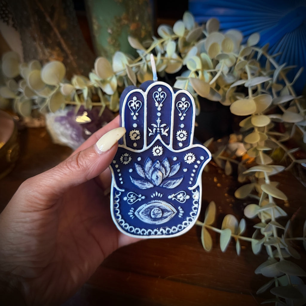 Hand holding a blue Hamsa-shaped candle with decorative elements in the background