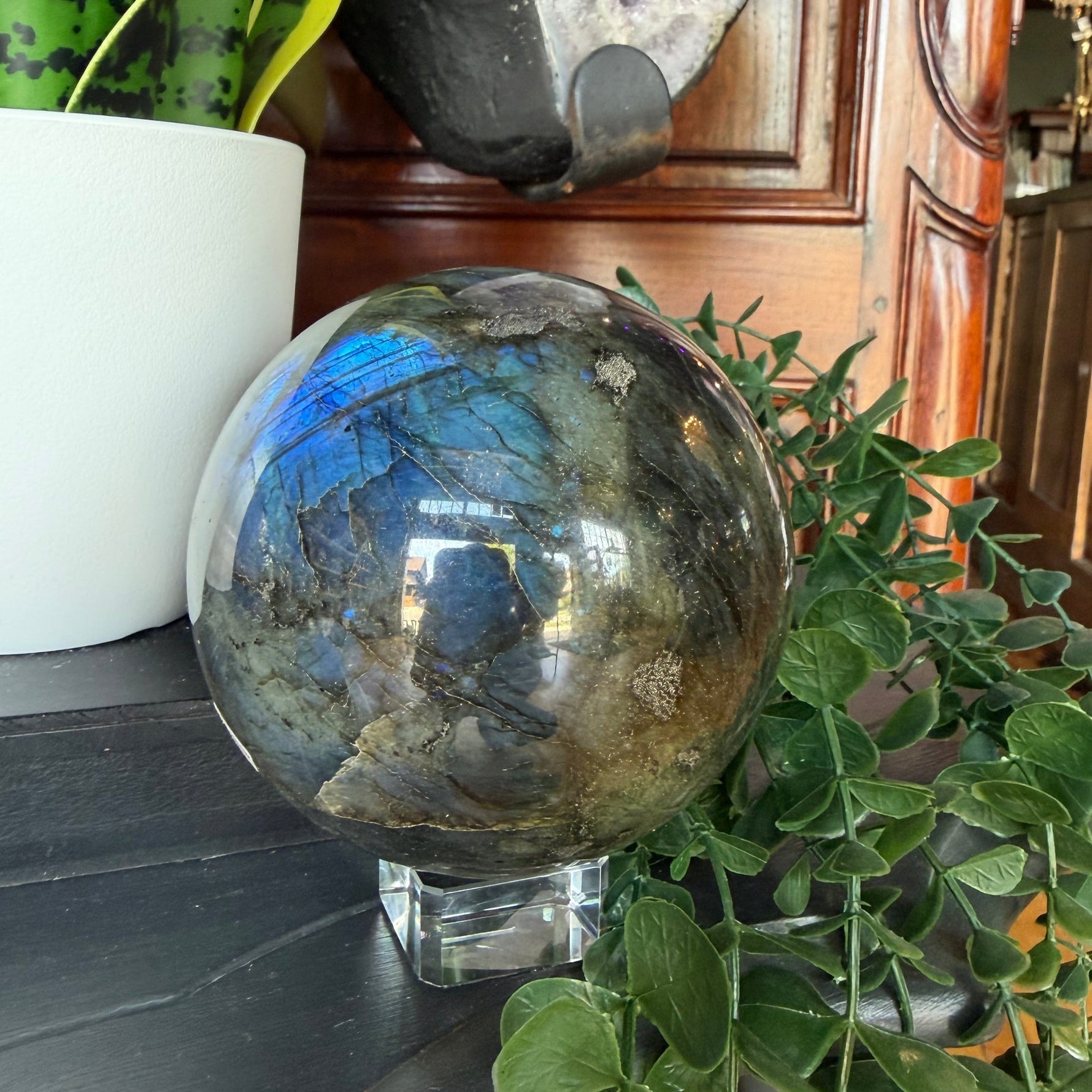 Crystal ball on a surface with decorative items including a plant and crystals.