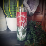 Decorative candle with red and green design on a shelf with plants and crystals.