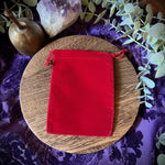 Red velvet pouch on a wooden board with crystals and plants on a purple fabric background