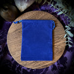 Blue pouch on a wooden plate with crystals and plants on a purple fabric background