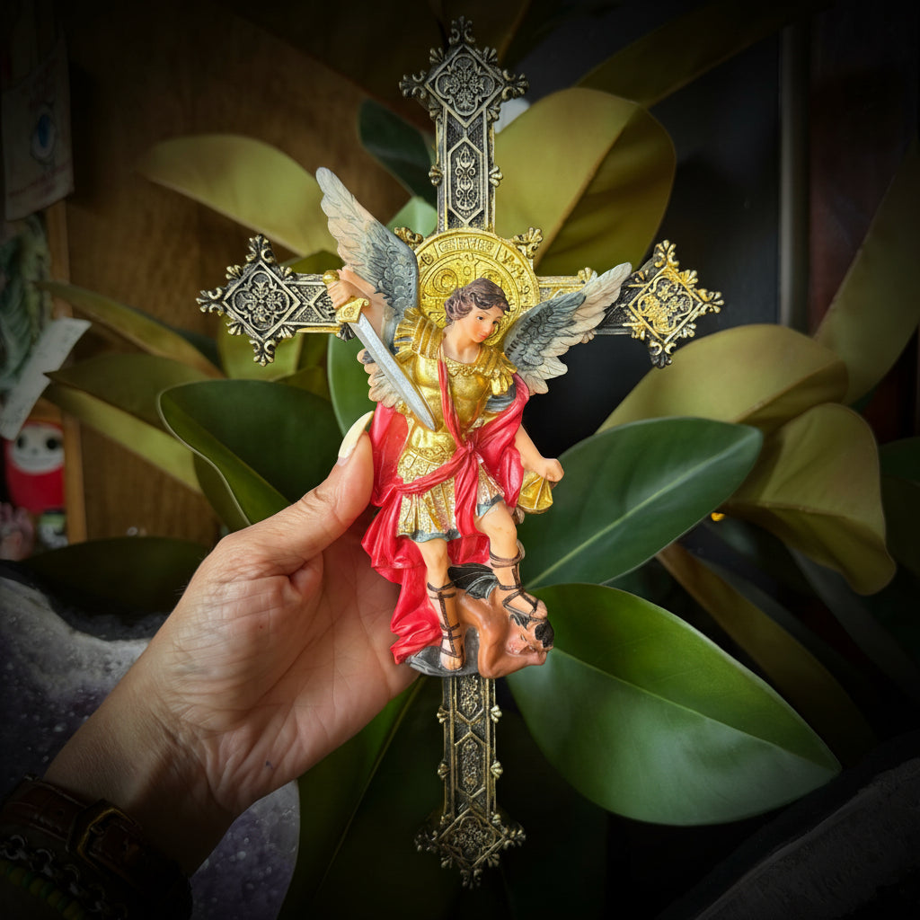 Hand holding a figurine of an angel with a cross, surrounded by green leaves and a textured surface.