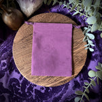 Purple velvet pouch on a wooden board with crystals and greenery on a purple fabric background