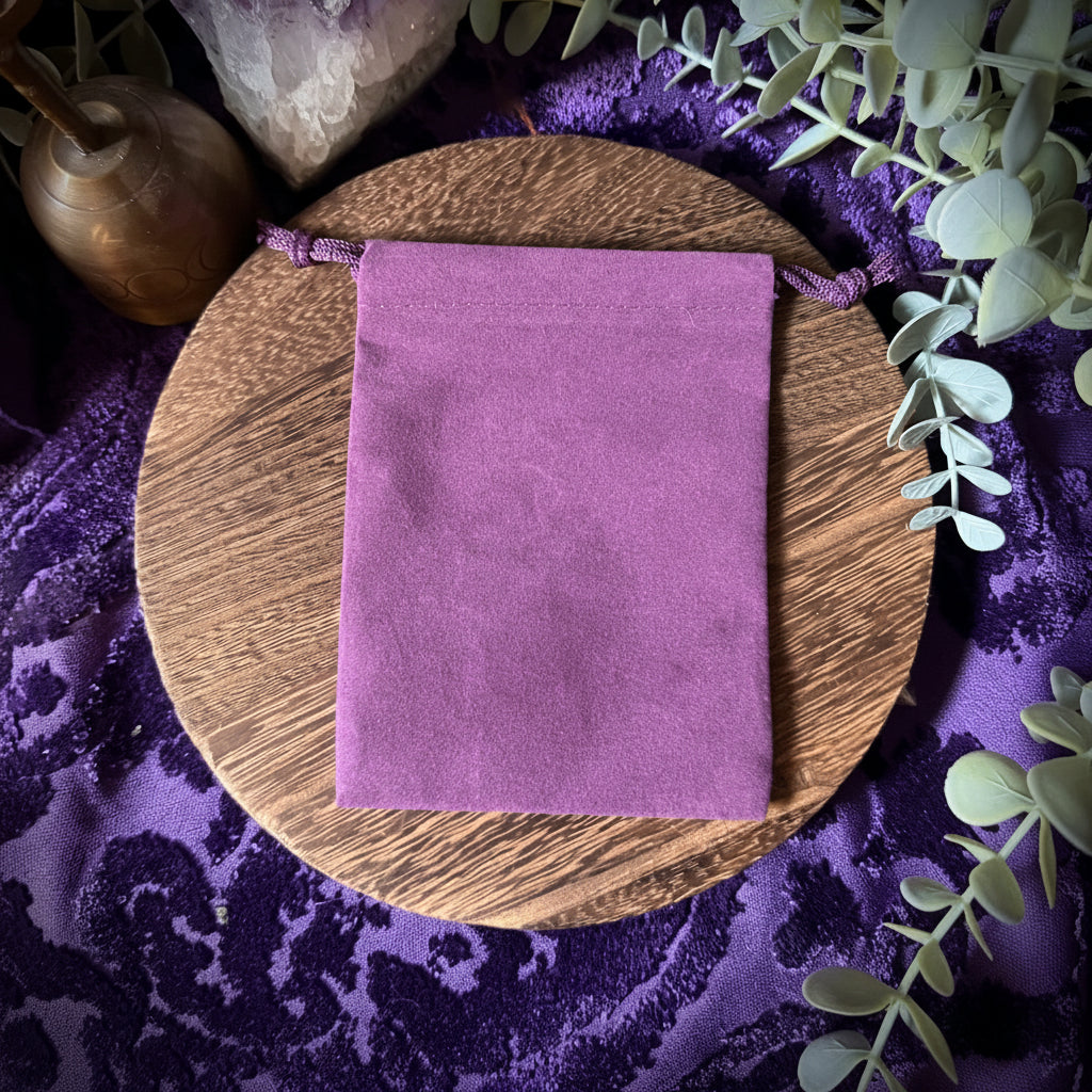 Purple velvet pouch on a wooden board with crystals and greenery on a purple fabric background